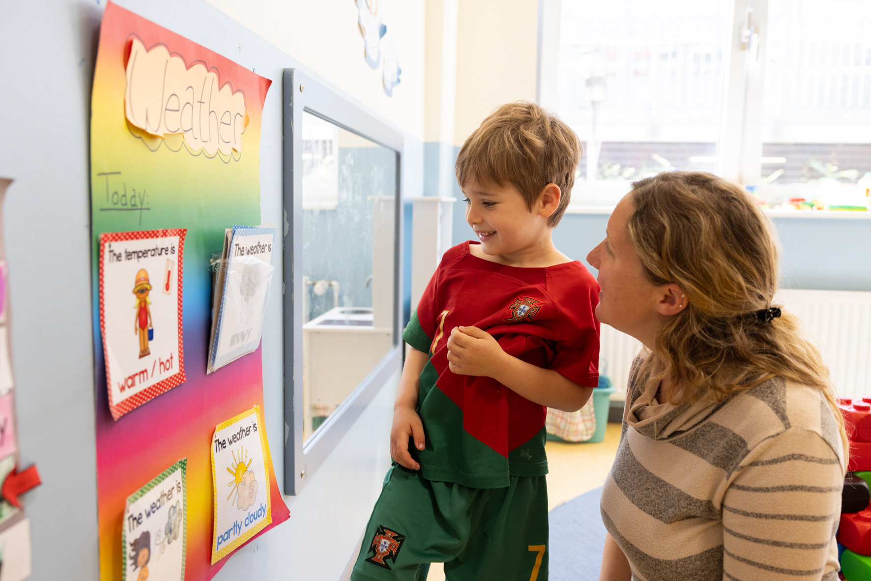 Kind steht mit Lehrerin a der Wand und lernt Wetterarten in der Phorms Kita Hamburg
