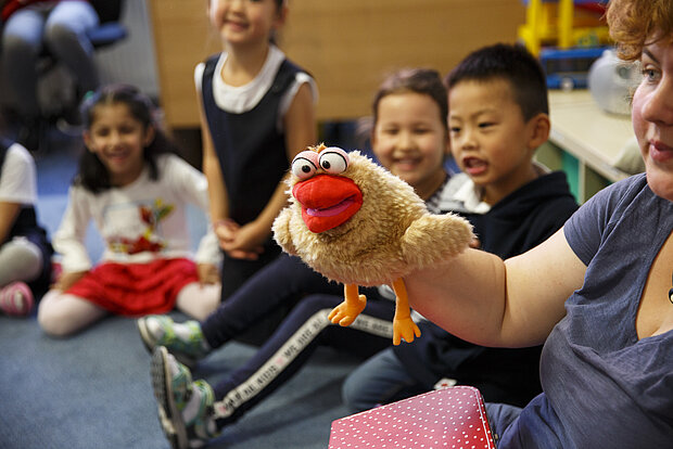 lächelnde Kinder sitzen mit Erzieherin mit Puppe im Kreis in der Phorms Reception Hamburg