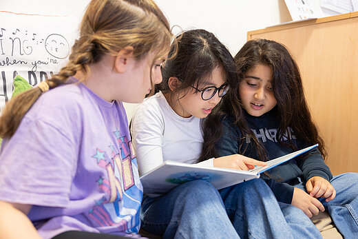 Drei Kinder sitzen nebeneinander uns lesen gemeinsam ein Buch