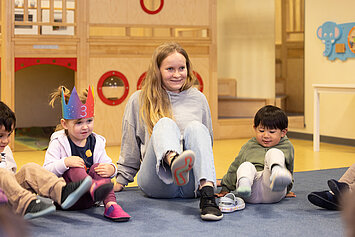 Phorms Hamburg Kita Kinder im Morgenkreis Eine lächelnde Erzieherin sitzt mit lächelnden Kindern im Morgenkreis während einer Aktivität in der Kita Phorms Hamburg