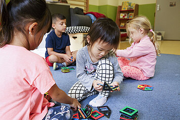Phorms Hamburg Kita Kinder Spielen Vier Kinder sitzen gemeinsam und Spielen mit Spielsteinen in der Phorms Kita Hamburg