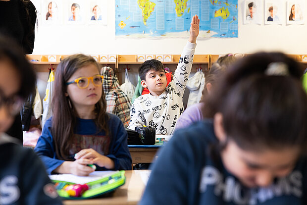 Schüler sitzen im Unterricht der Phorms Grundschule Hamburg. Ein Kind meldet sich und die anderen hören dem Unterricht zu.