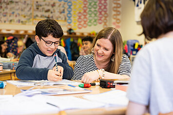 Phorms Hamburg Grundschule Lehrerin erklärt Schülerin Aufgabe Ein Kind sitzt im Klassenraum mit Lehrerin, die ihr etwas erklärt.