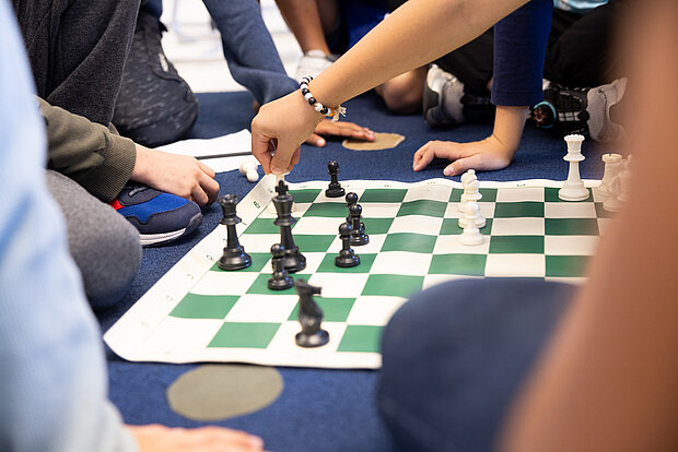 Eine Gruppe Kinder sitzen auf dem Boden und zwei spielen Schach, während die anderen zugucken in der Phorms Grundschule Hamburg