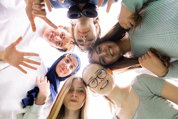 Sechs Schüler stehen im Kreis und gucken runter auf eine Kamera im Phorms Gymnasium Hamburg