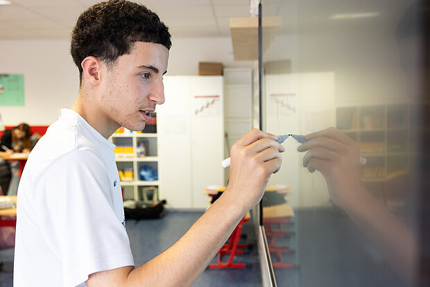 Ein Schüler steht im Unterricht am Smartboard und schreibt etwas im Phorms Gymnasium Hamburg