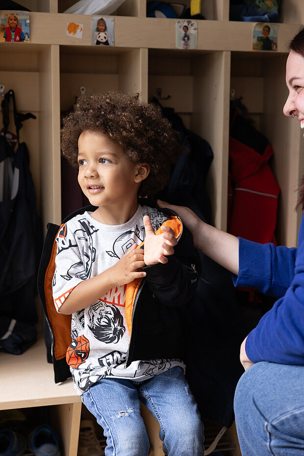 Kita-Kind zieht Jacke an zum raus Gehen in der Phorms Kita Hamburg