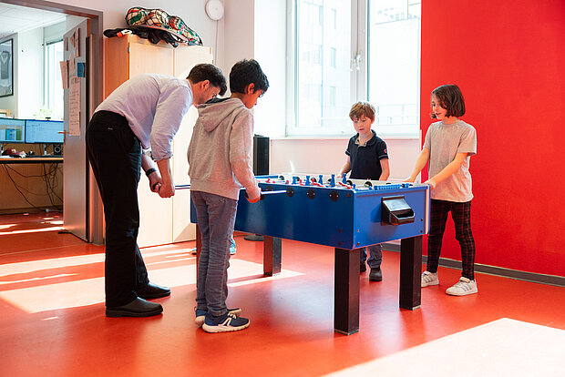 Drei Kinder und ein Lehrer spielen gemeinsam an einem Kicker Tisch in der Phorms Grundschule Hamburg 