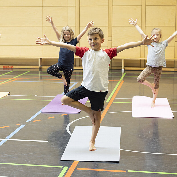 Kinder sind in der Sporthalle auf Yoga Matten und machen eine Yoga Figur in der Phorms Grundschule Hamburg