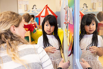 Kind steht mit Erzieherin und sie reden und lernen etwas in der Phorms Hamburg Kita