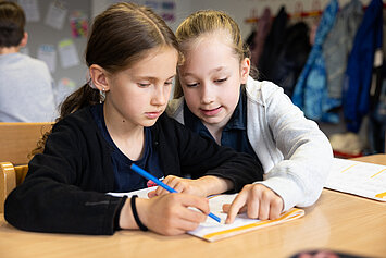 Phorms Hamburg Grundschule Schüler helfen einander Zwei Kinder bearbeiten Aufgaben im Unterricht und das eine Kind erklärt dem anderen etwas.