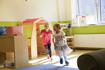 Phorms Hamburg Kita Kinder rennen Zwei Mädchen rennen gemeinsam lachend durch einen Raum der Phorms Kita Hamburg