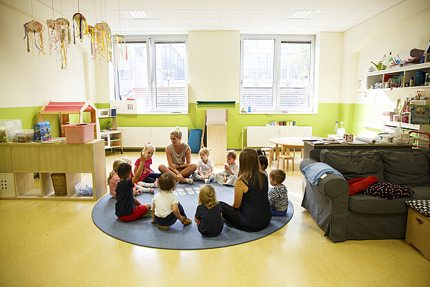 Eine kleine Gruppe Kinder sitzt mit zwei Erzieherinnen im Morgenkreis und unterhalten sich