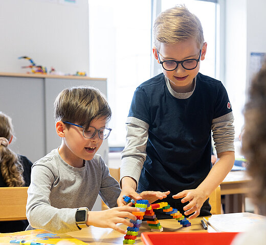 Zwei Kinder sitzen zusammen an einem Tisch und spielen mit Lego steinen in der Phorms Grundschule Hamburg