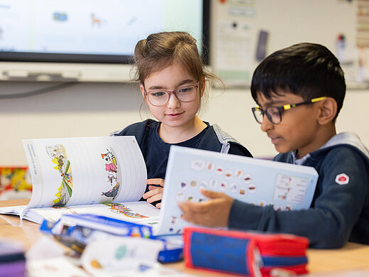 Zwei lächelnde Kinder reden miteinander, während sie in ihren Heften blättern.