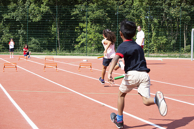 Kinder machen Sportunterricht draußen und rennen einen Staffellauf auf dem Sportplatz der Phorms Grundschule Hamburg